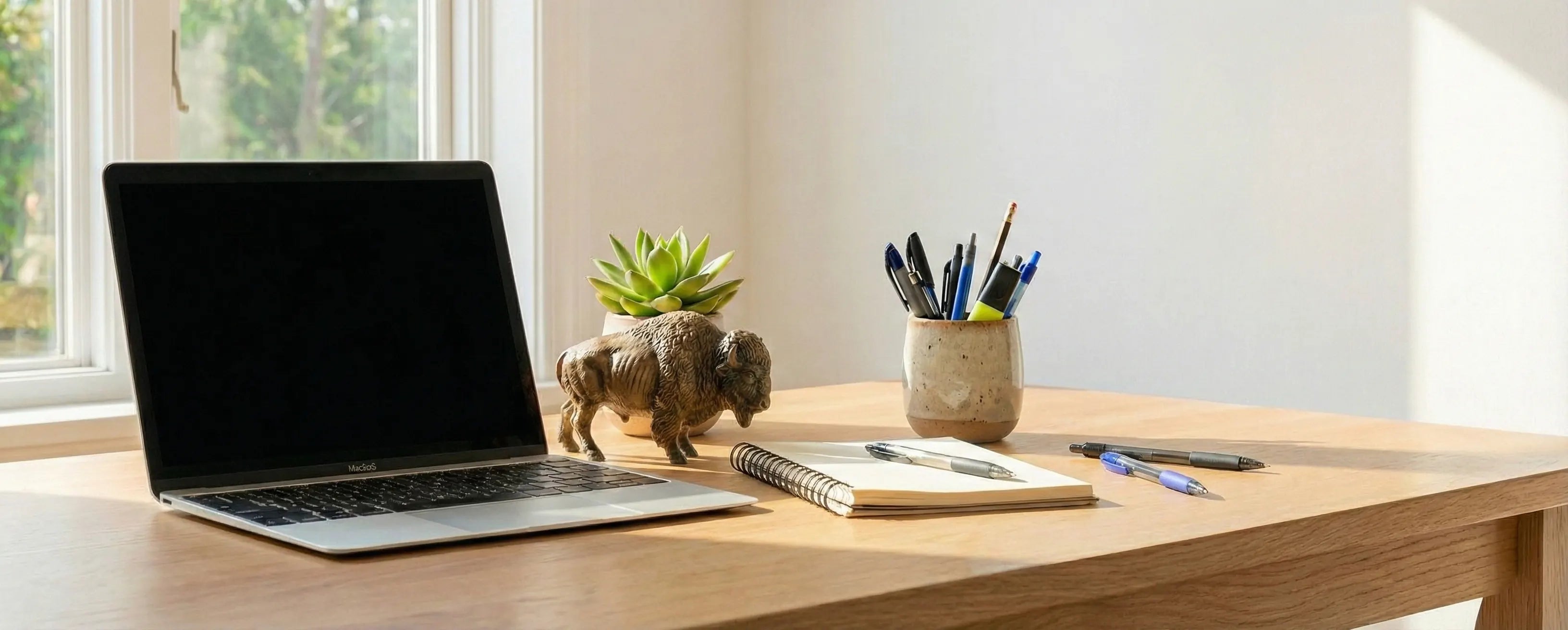 Calm home office desk featuring a wooden bison figurine and green plants. Biophilic design workspace to reduce stress and bring nature indoors