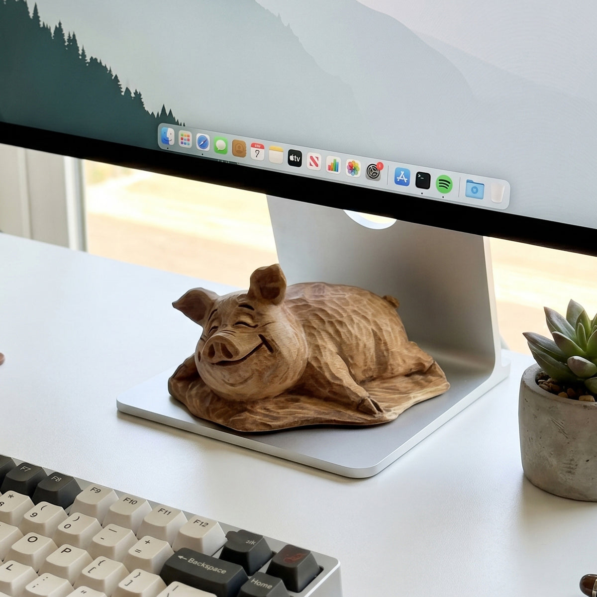 Wooden pig figurine on a desk beside a keyboard and monitor