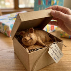 Hand opening a small gift box revealing the wooden pig figurine inside