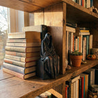 Wooden Grim Reaper figurine displayed on a wooden bookshelf next to books and a small plant