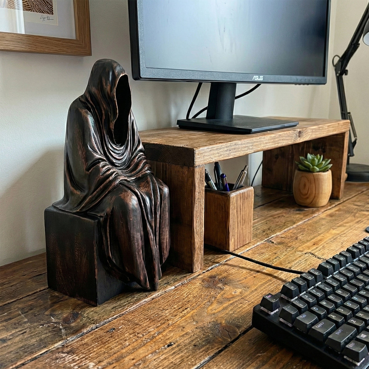 Wooden Grim Reaper figurine displayed on a desk next to a computer monitor and keyboard