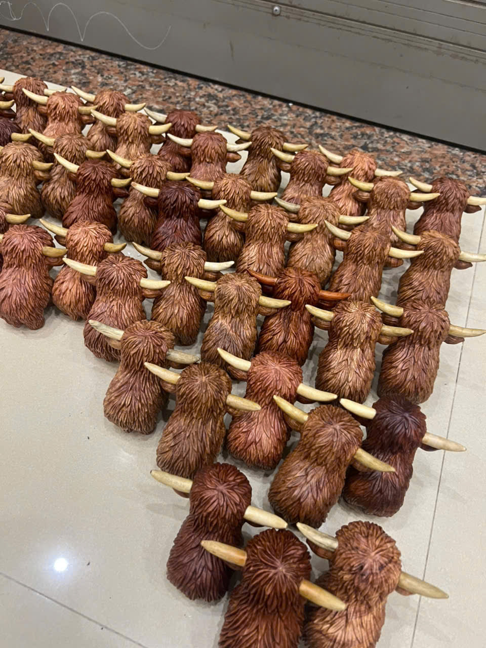 Row of small brown highland cow figurines with large ears and long tails on a tiled floor.